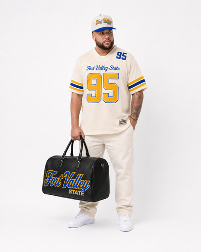 Fort Valley State Legacy Jersey male campaign image in cream jersey with cap and travel bag